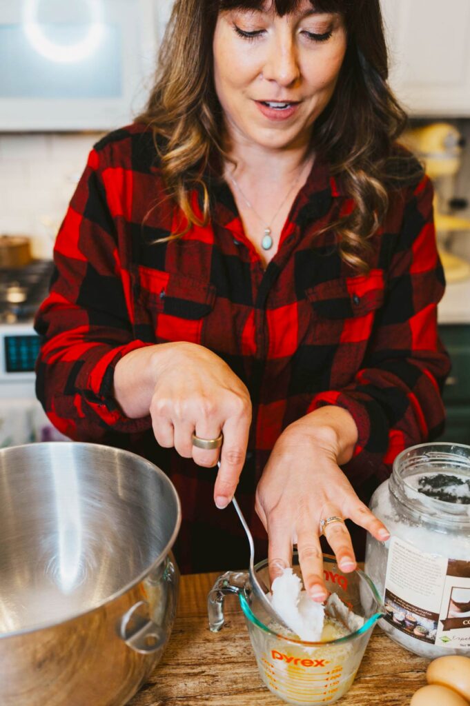 A woman scooping coconut oil into a measuring cup.