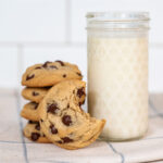 A stack of chocolate chip cookies next to a glass of milk.