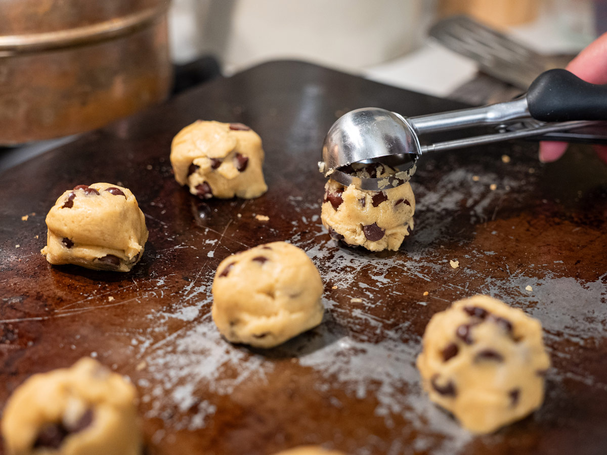 Chocolate chip cookie dough balls being placed onto a baking tray.