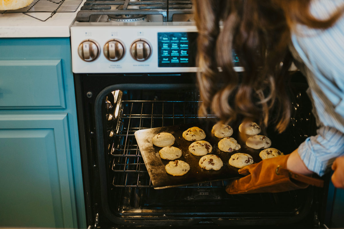 A woman pulling chocolate chip cookies out of the oven.