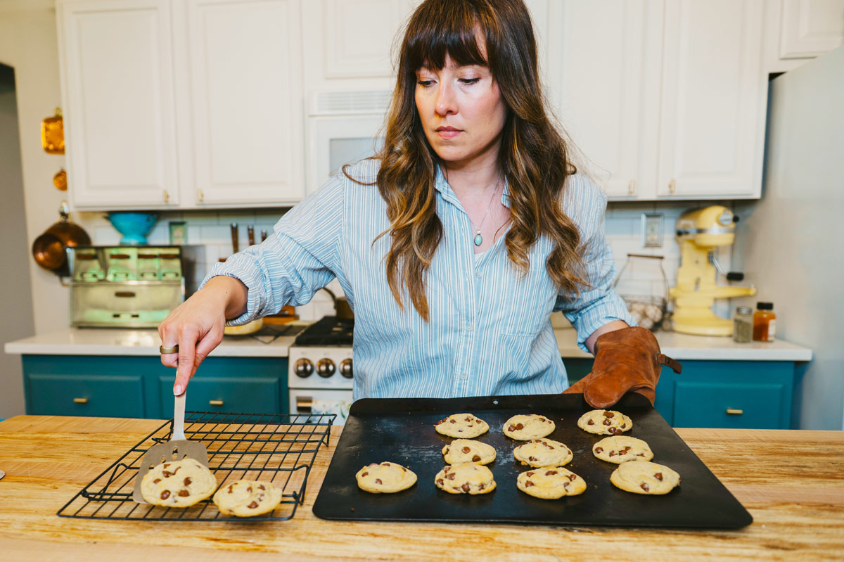 A woman moving chocolate chip cookies onto a cooling rack.