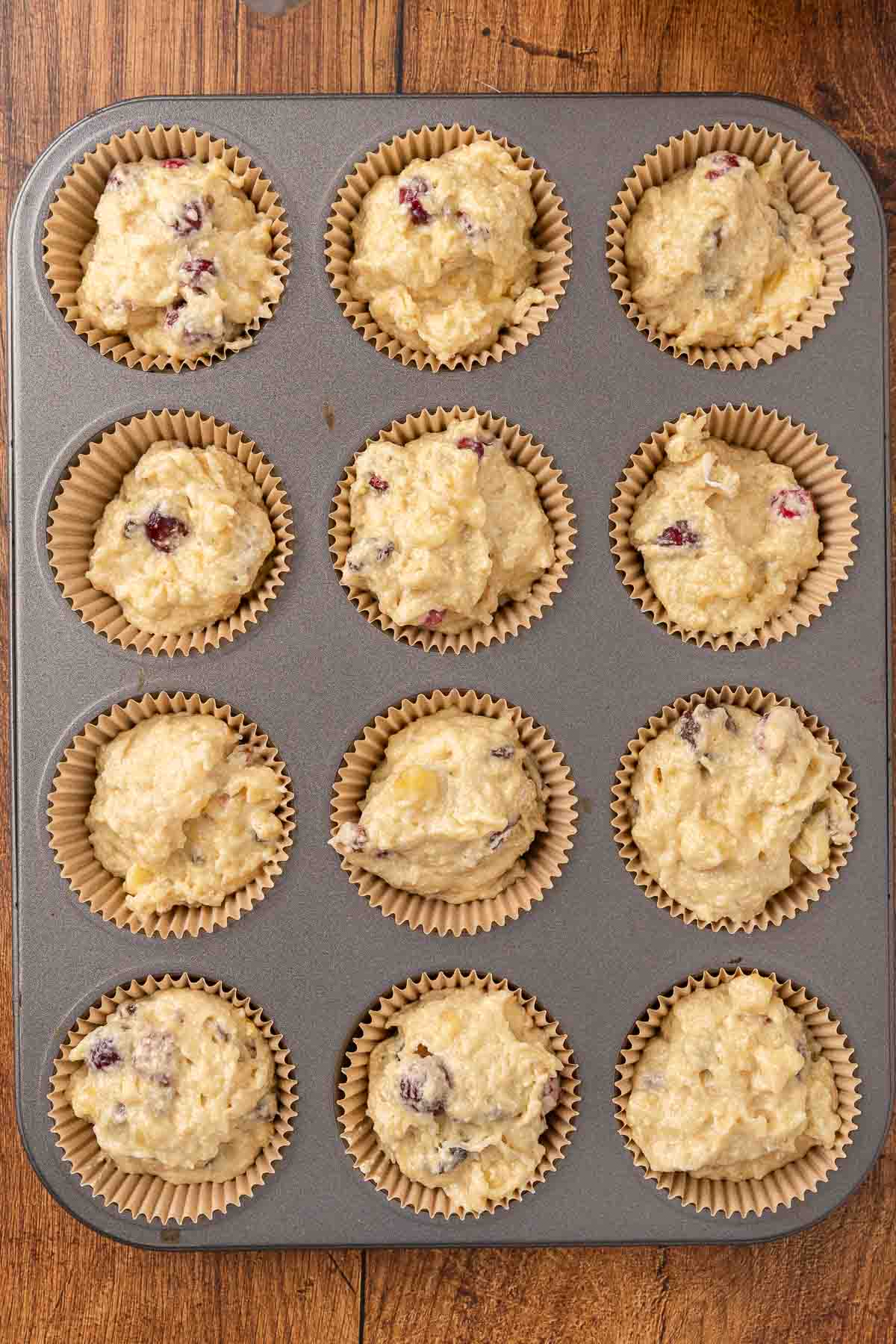 Cranberry muffin batter in a muffin tin.