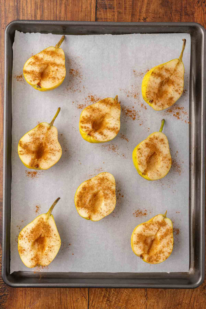 Cinnamon dusted pear halves on a baking tray.
