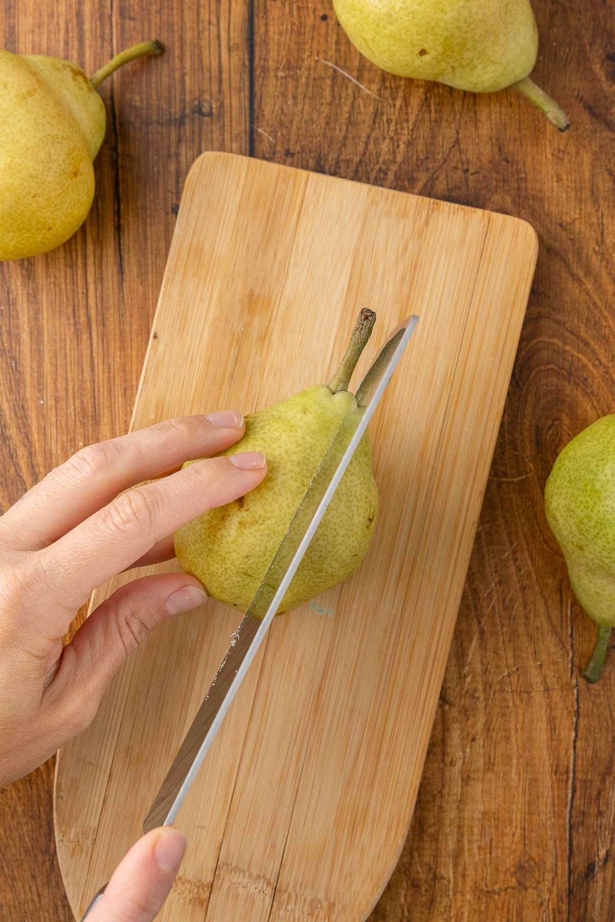 A pear being cut in half on a cutting board.