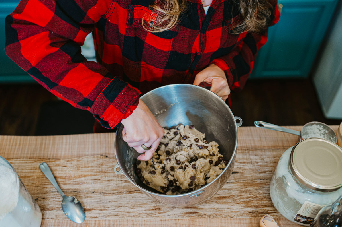 A woman mixing together chocolate chip cookie dough.