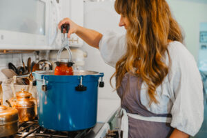 Woman pulling jar of home canned tomato sauce out of pressure canner