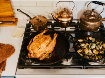 A roasted chicken and sauteed vegetables on a stovetop.