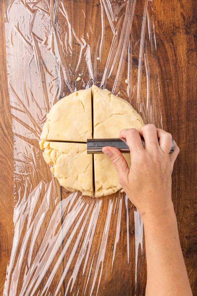 A hand using a bench knife to divide a ball of pie crust dough into four equal pieces.