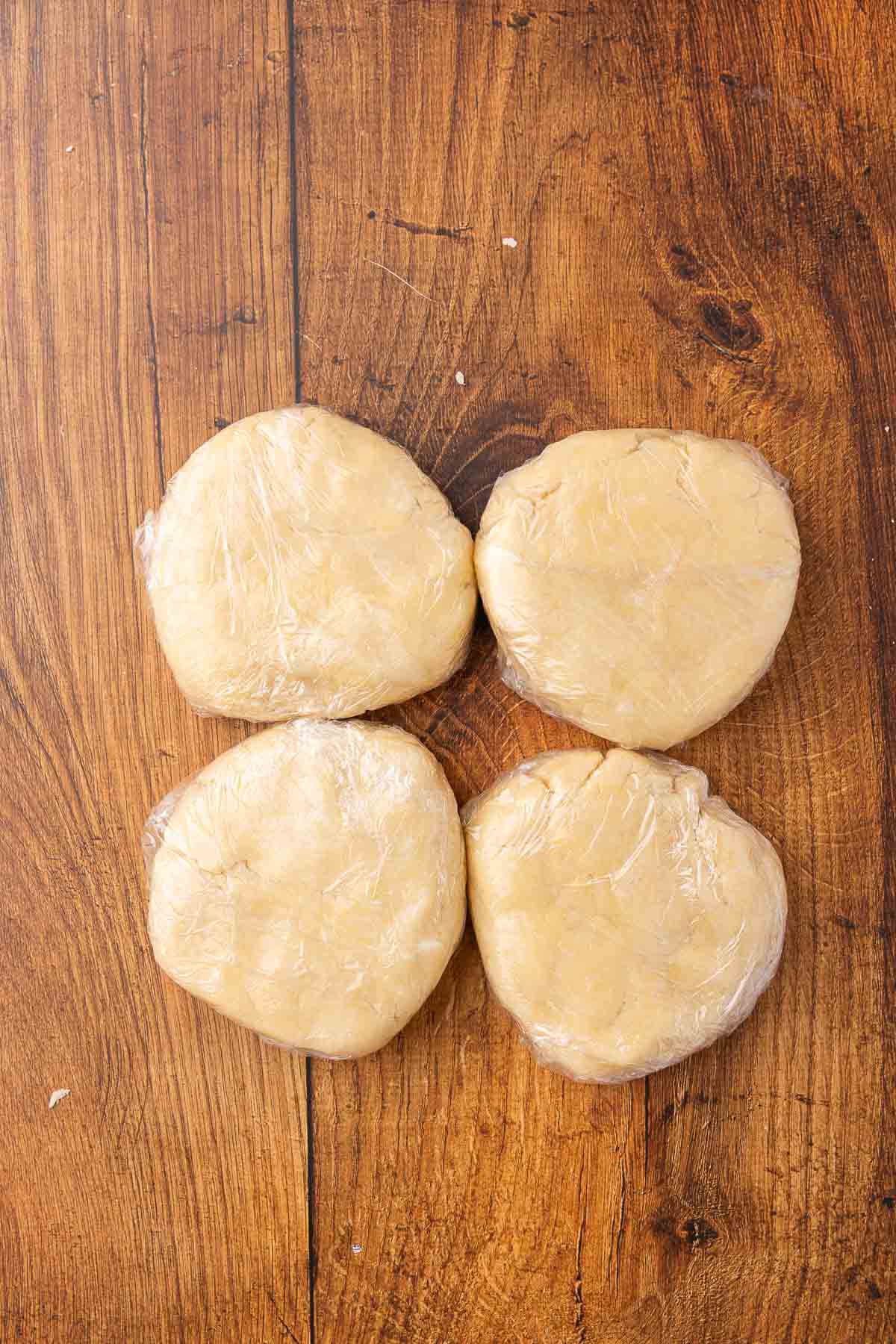 Four balls of pie crust dough wrapped in plastic wrap for storage.