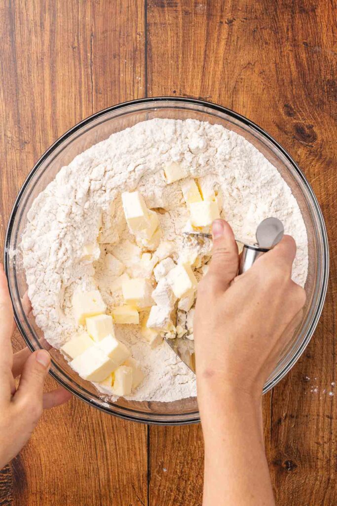 A hand using a pastry cutter to cut butter into flour mixture.
