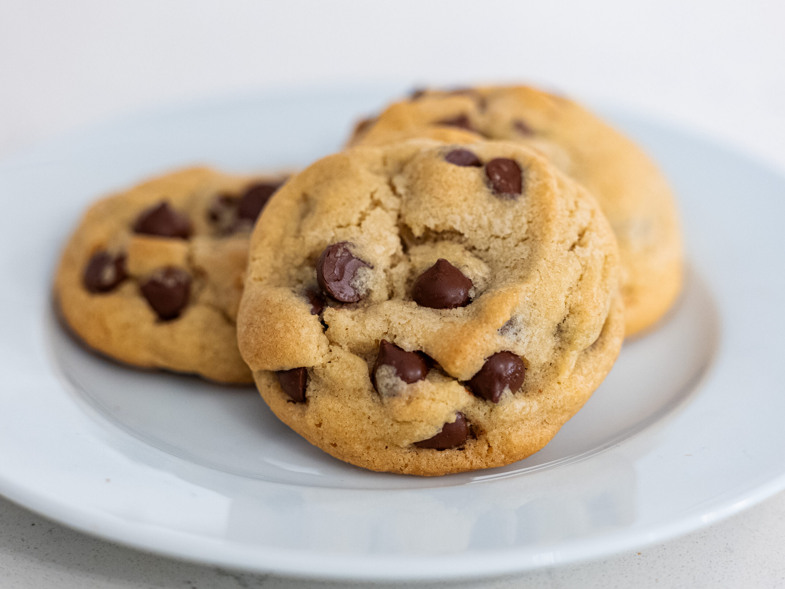 Three homemade chocolate chip cookies on a white plate