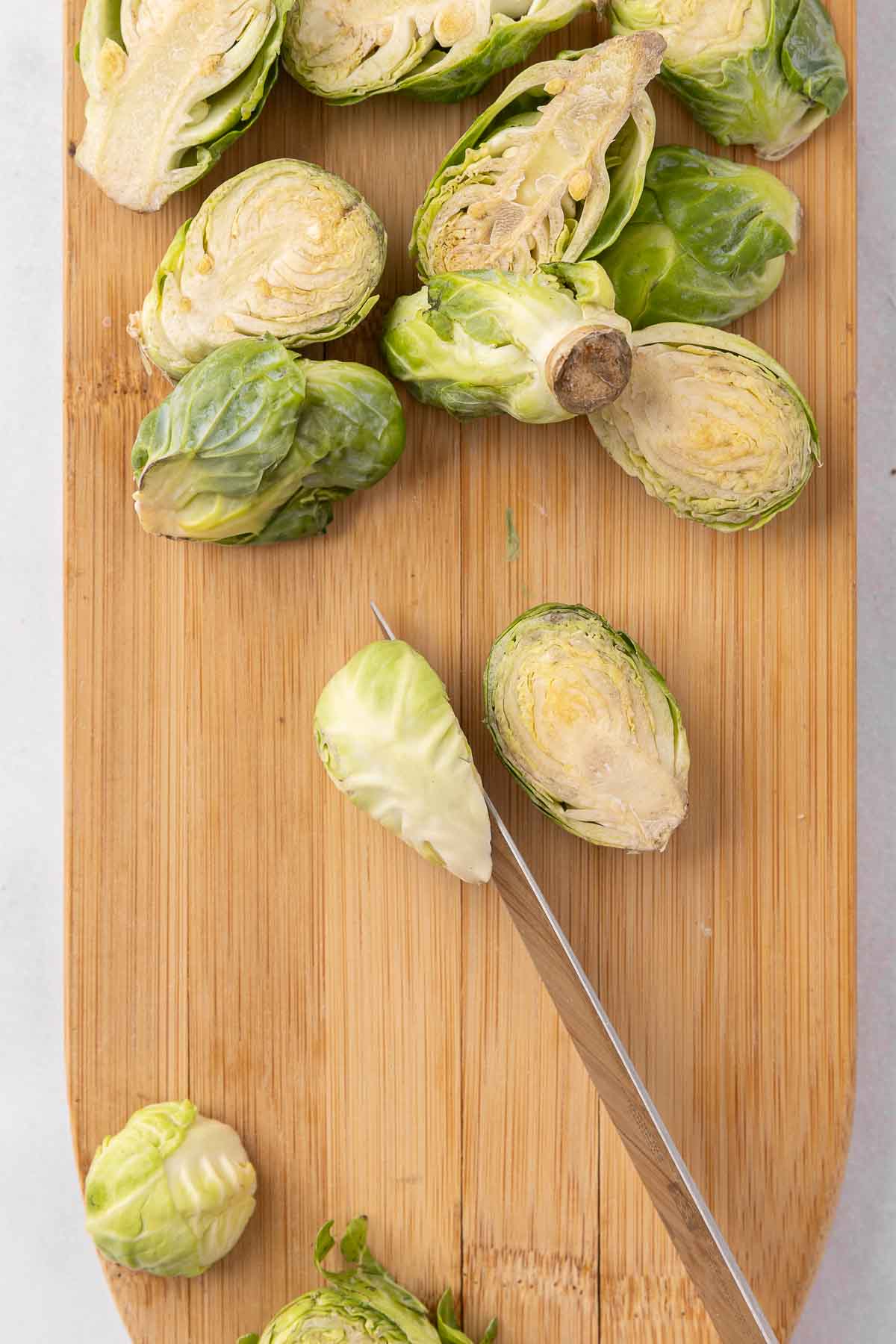 Brussels sprouts being cut in half on a wooden cutting board.