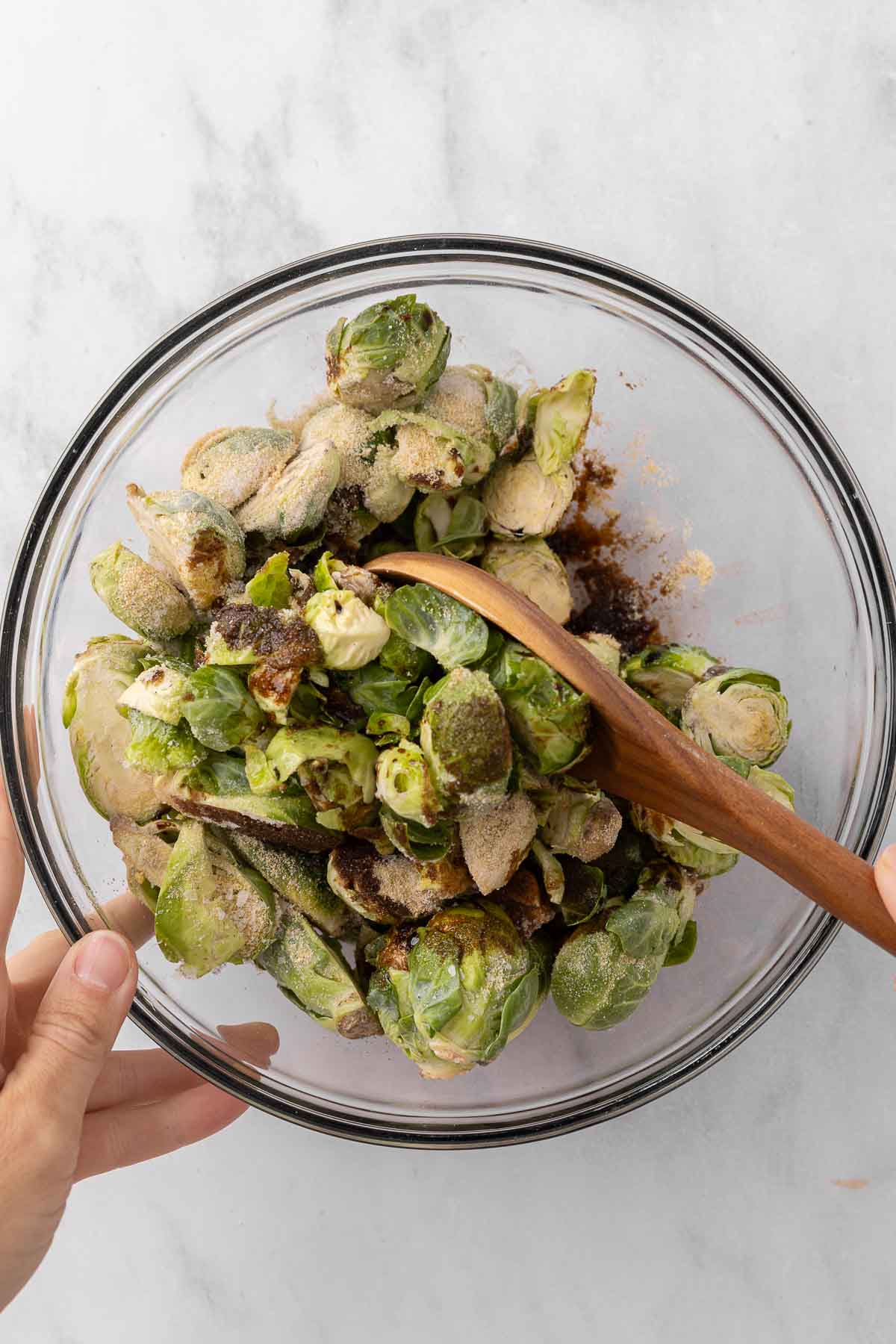 Mixing Brussel sprouts in a glass bowl with seasonings.
