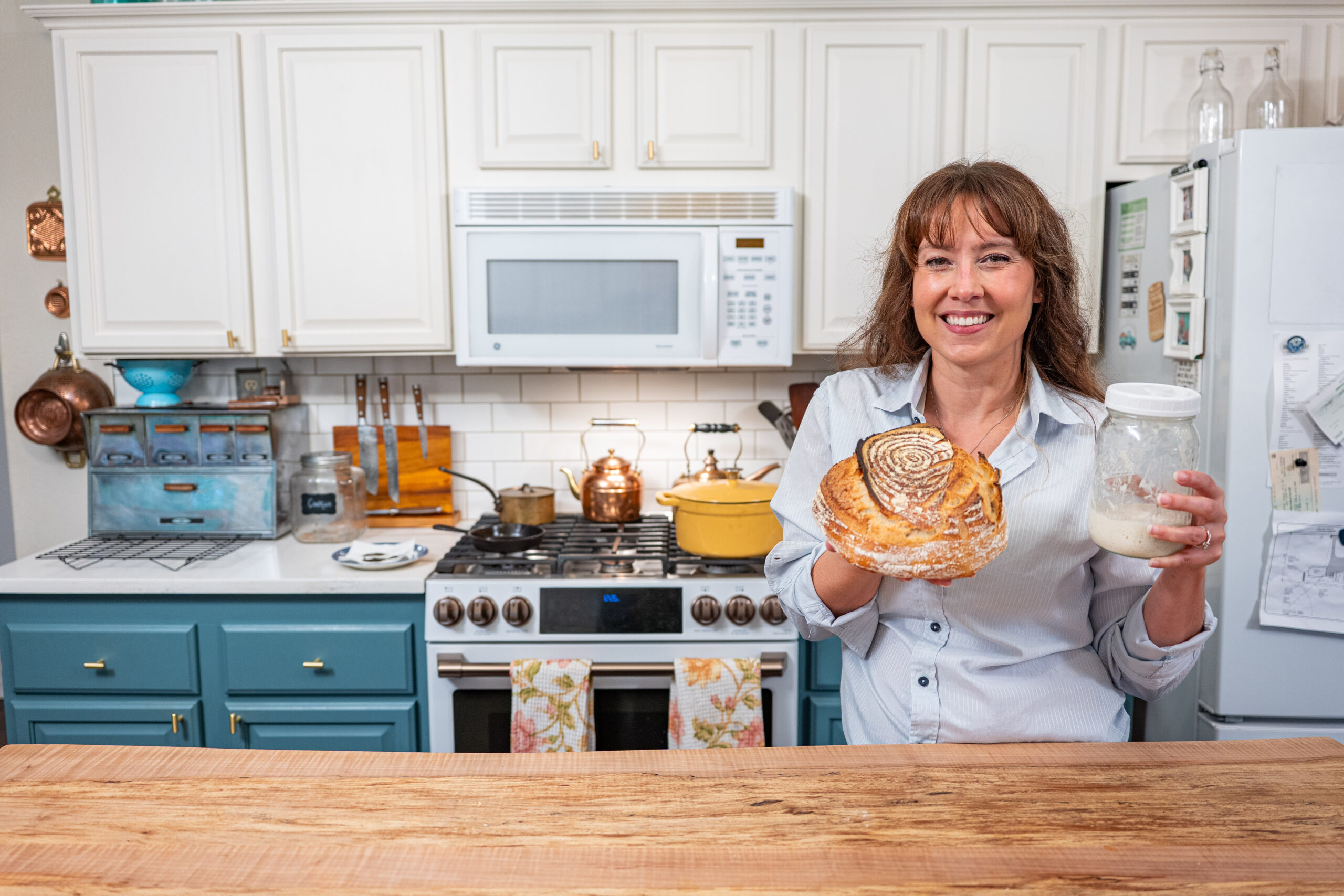Woman in kitchen holiding a jar of sourdough starter and a loaf of sourdough artisan bread