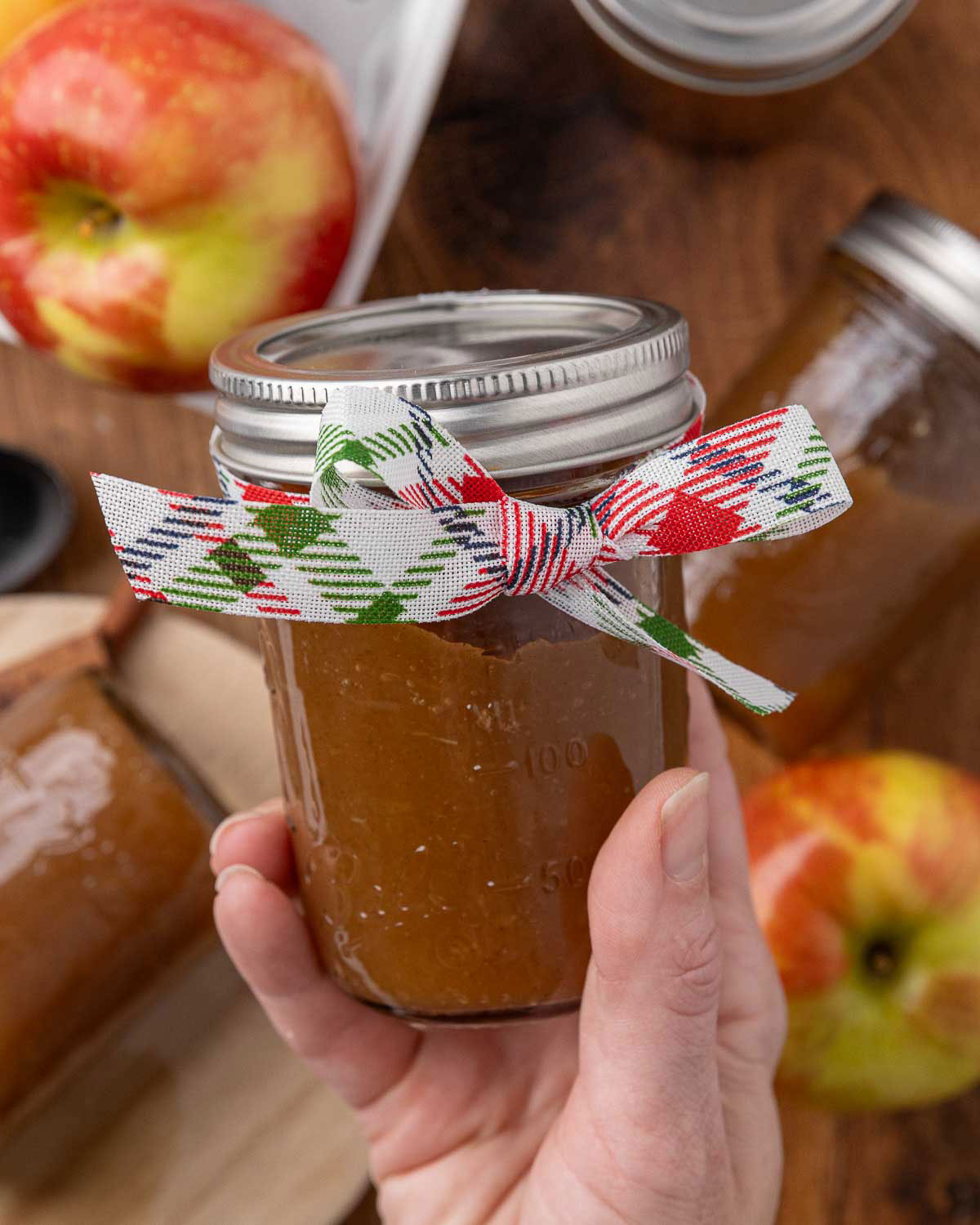 A hand holding a jar of apple butter decorated with a bow.