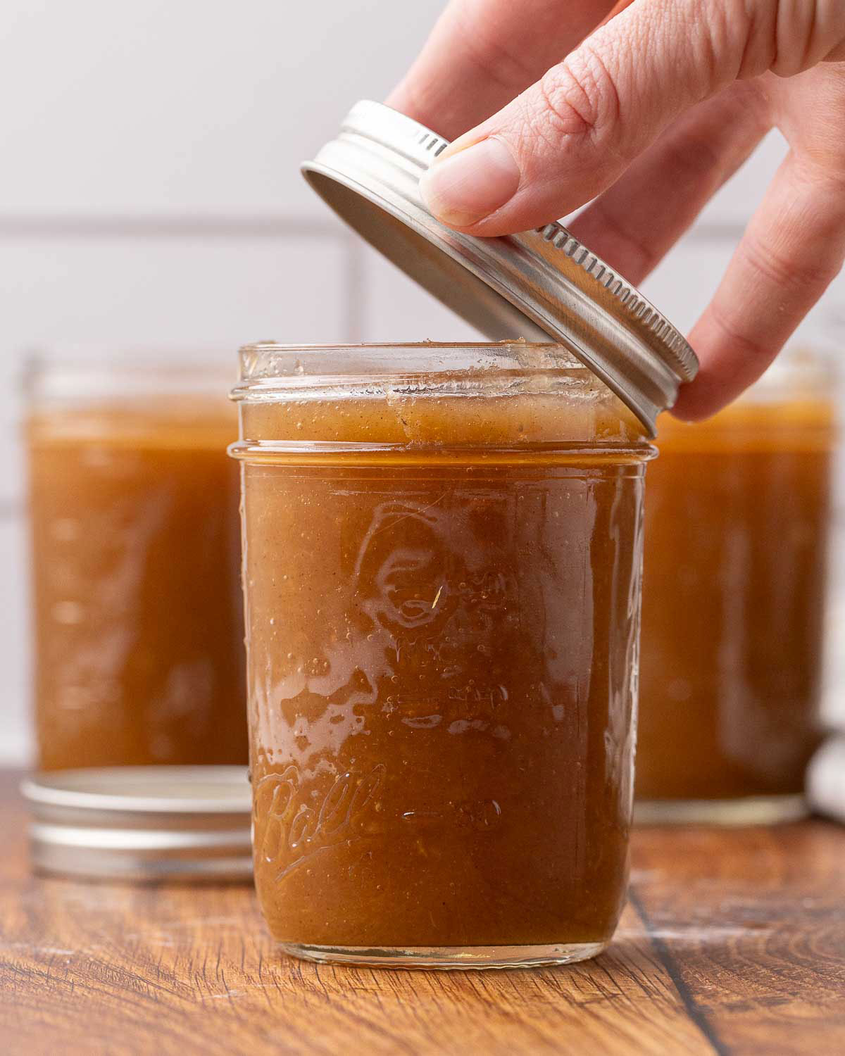 A hand placing a lid on a jar of apple butter.