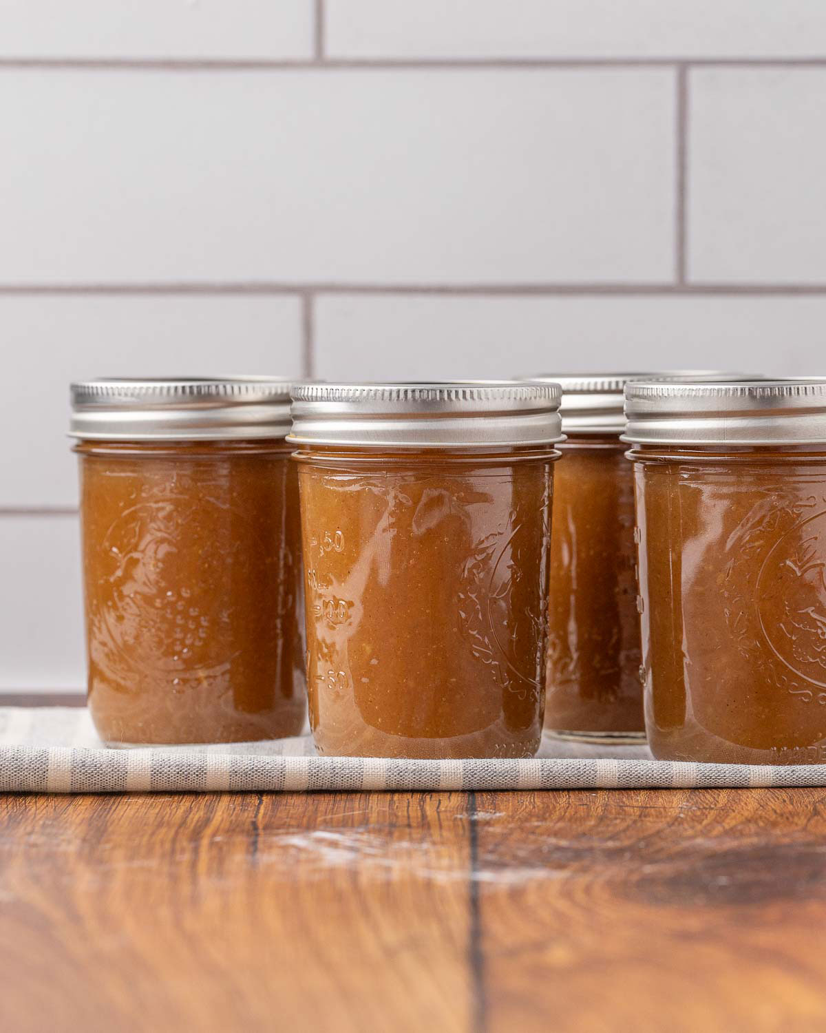 Jars of finished apple butter cooling on a towel.
