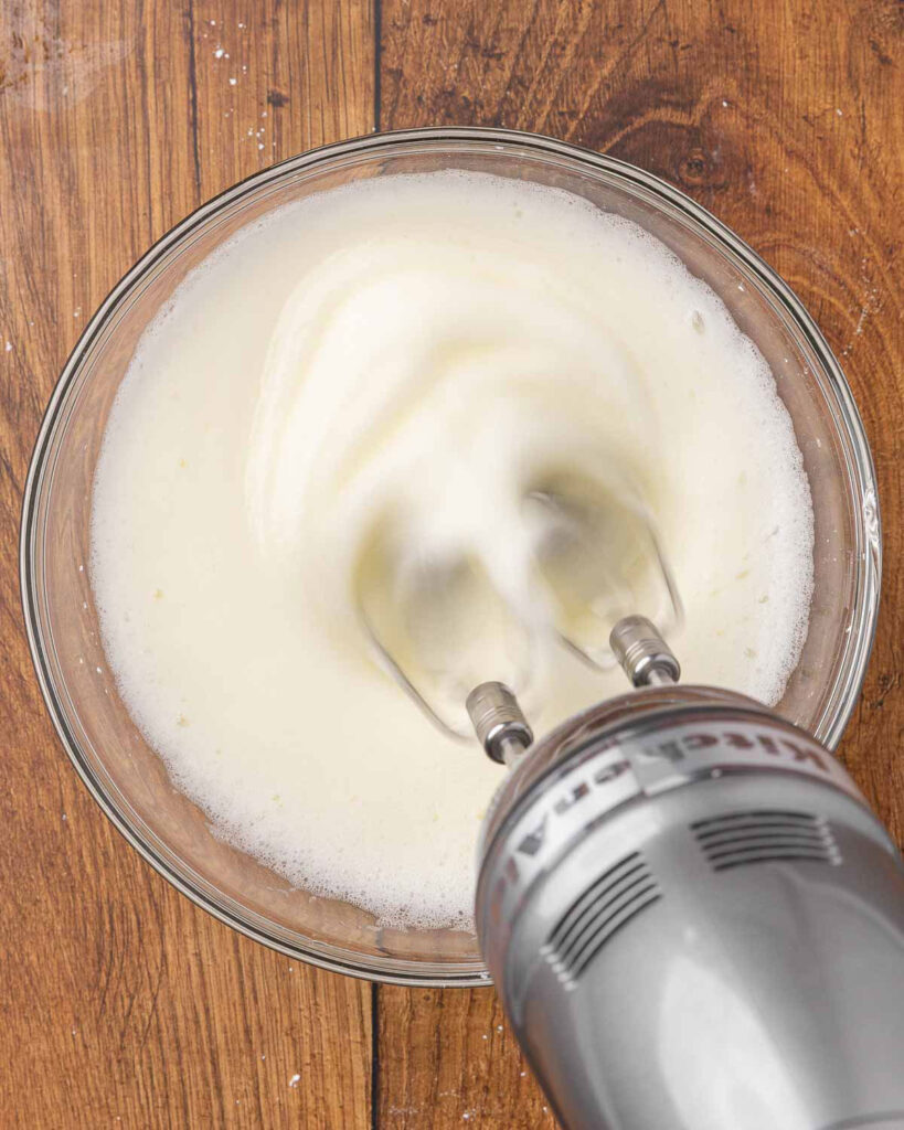 A hand mixer whipping egg whites into stiff peaks.
