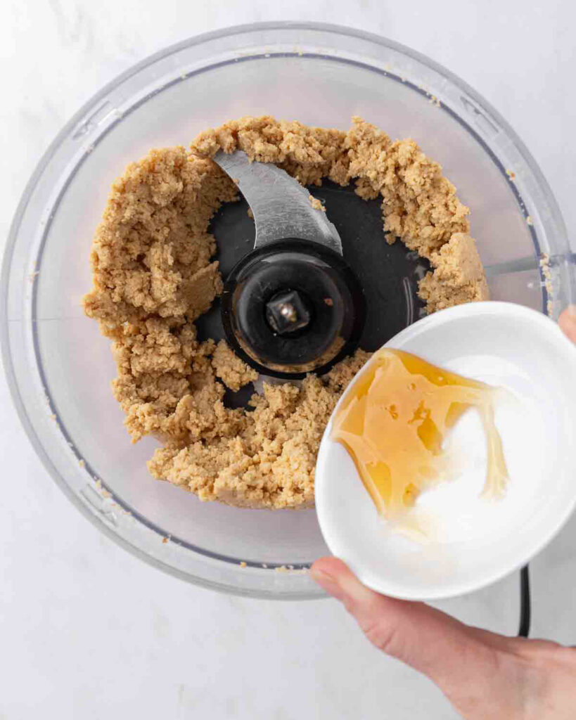 Adding honey to a food processor filled with freshly ground peanut butter.