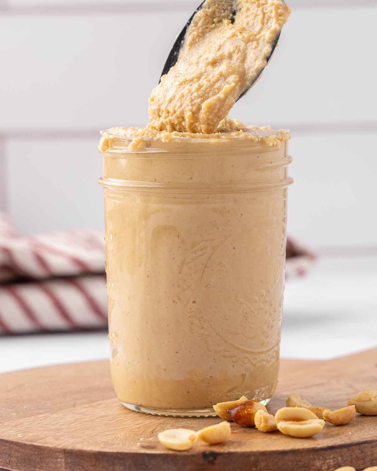 A pint jar filled with freshly ground peanut buttter with a spoon lifting a serving to show texture.