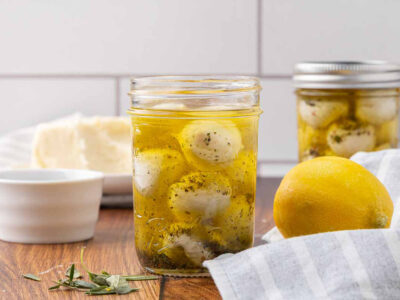 One opened and one sealed jar of marinated mozzarella balls sitting on a counter.