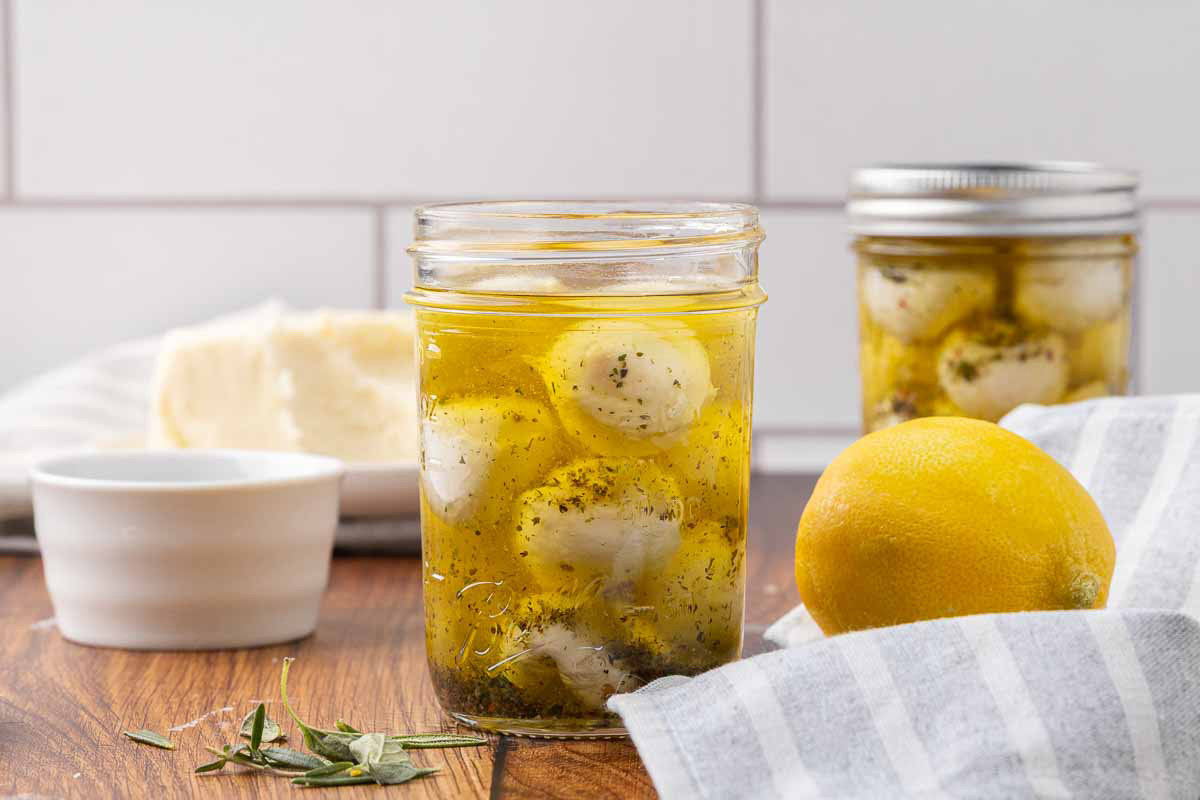 One opened and one sealed jar of marinated mozzarella balls sitting on a counter.