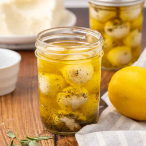 One opened and one sealed jar of marinated mozzarella balls sitting on a counter.