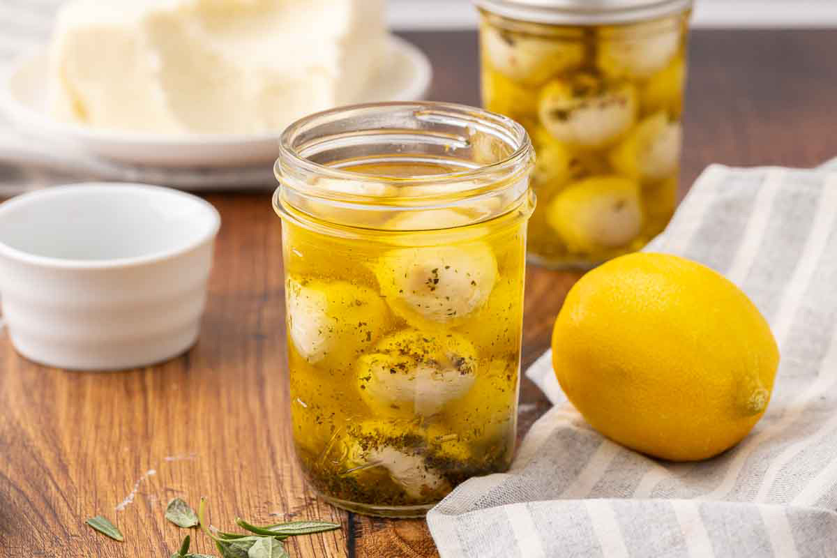 One opened and one sealed jar of marinated mozzarella balls sitting on a counter.