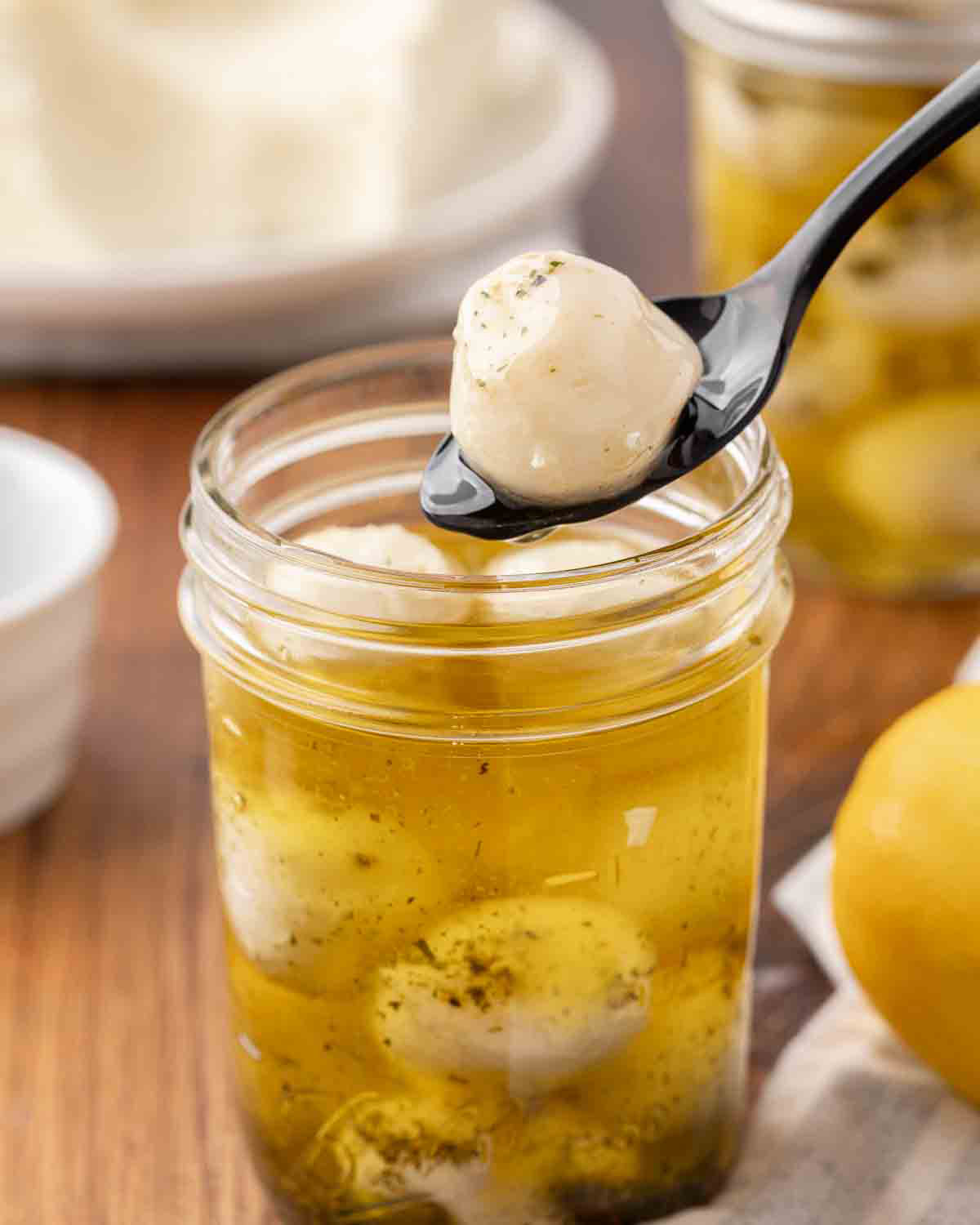 A spoon lifting a mozzarella ball from a jar to show texture.