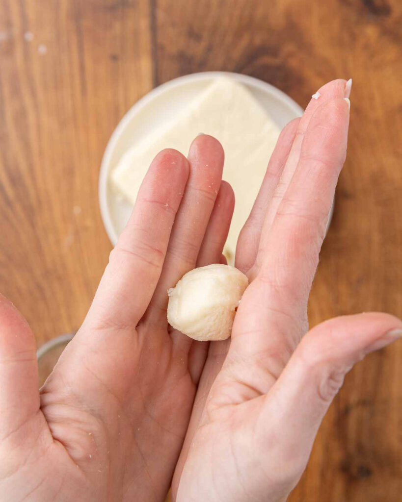 Hands rolling mozzarella into a ball.
