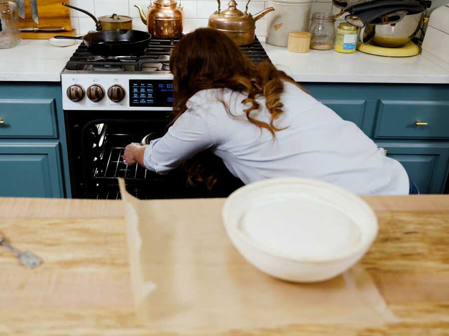 A woman placing a Dutch oven into an oven to preheat.