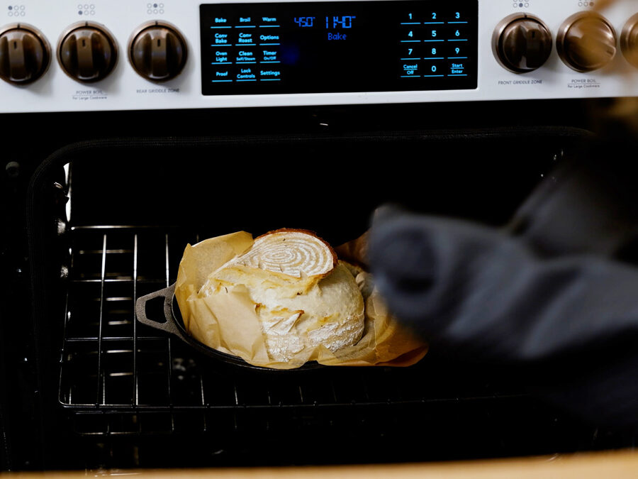 A woman taking the lid off a loaf of sourdough bread.