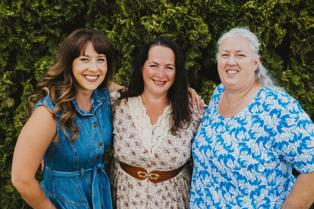 Three woman smiling with their arms around each other in a row