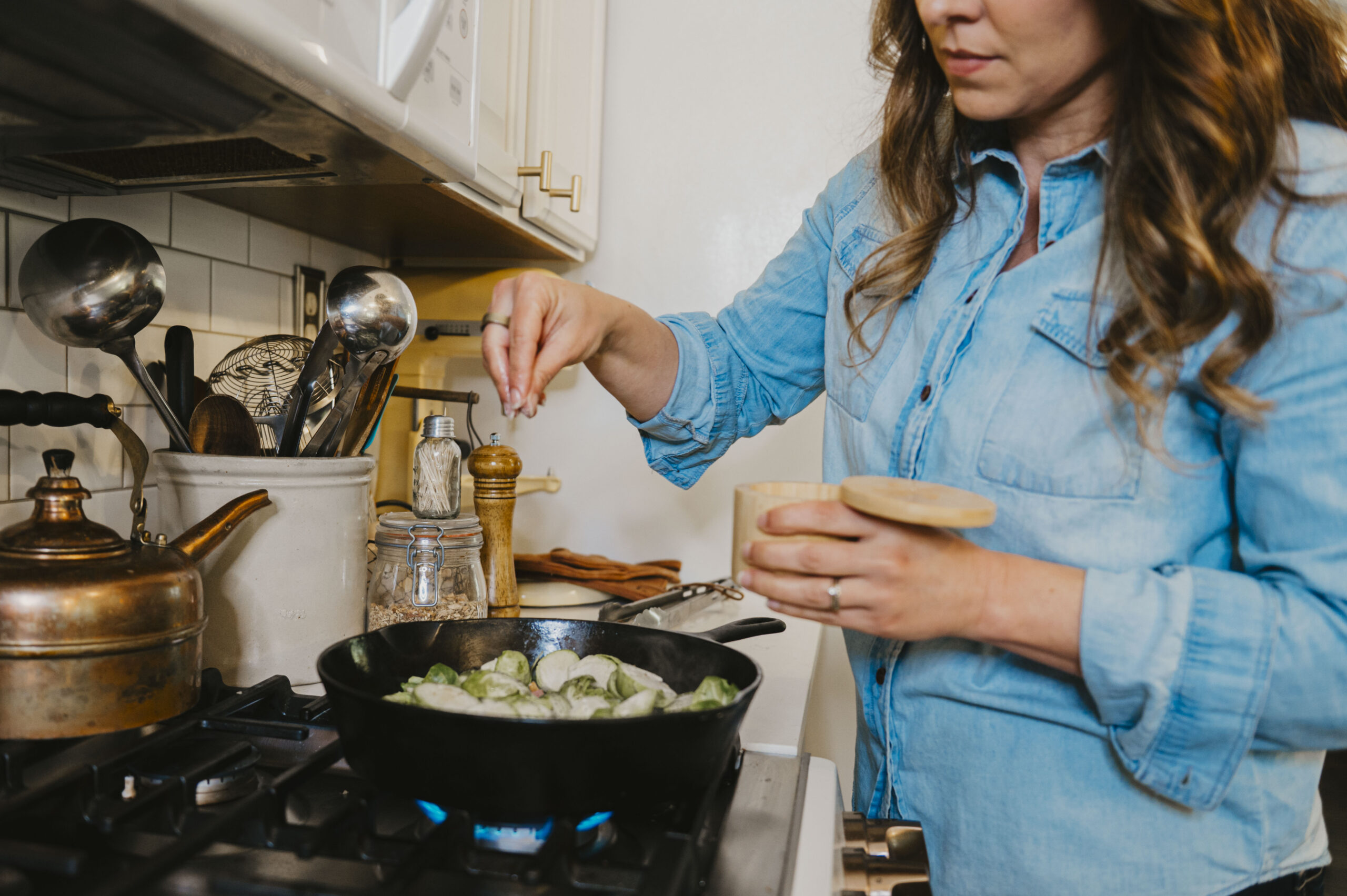 A women sprinkling salt onto a cast iron skillet of brussel sprouts on the stove top