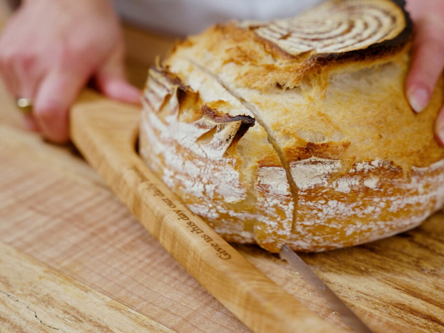 A loaf of sourdough bread being sliced with a knife.