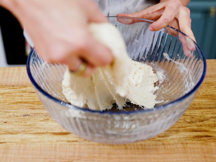 A woman doing "stretch and folds" to sourdough boule dough.