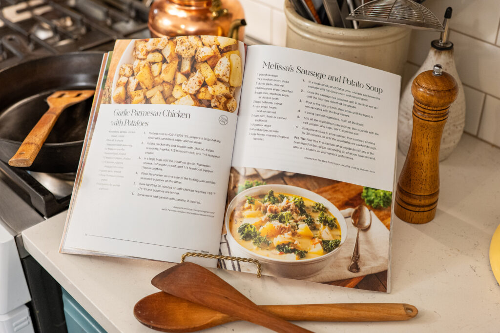 A magazine with recipes at the kitchen stove with wooden spoons in front of it and a cast iron pan with a wooden spatula behind it. 