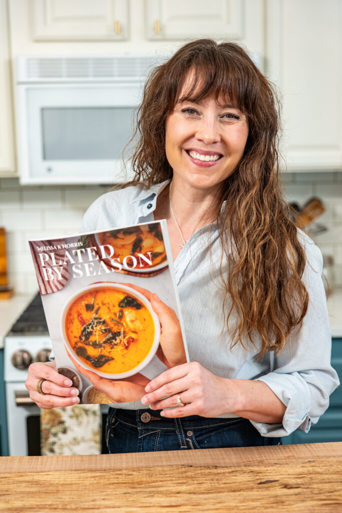 Woman smiling in her kitchen holding a copy of Plated by Season magazine