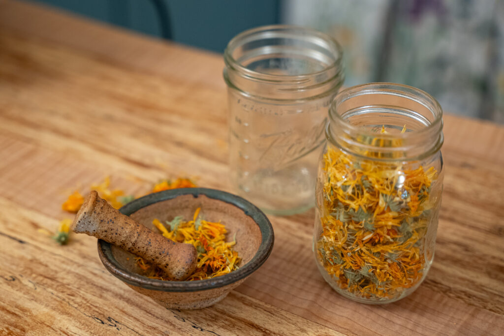 a jar of dried calendula on a kitchen counter with a mortar and pestal with calendula petals inside it