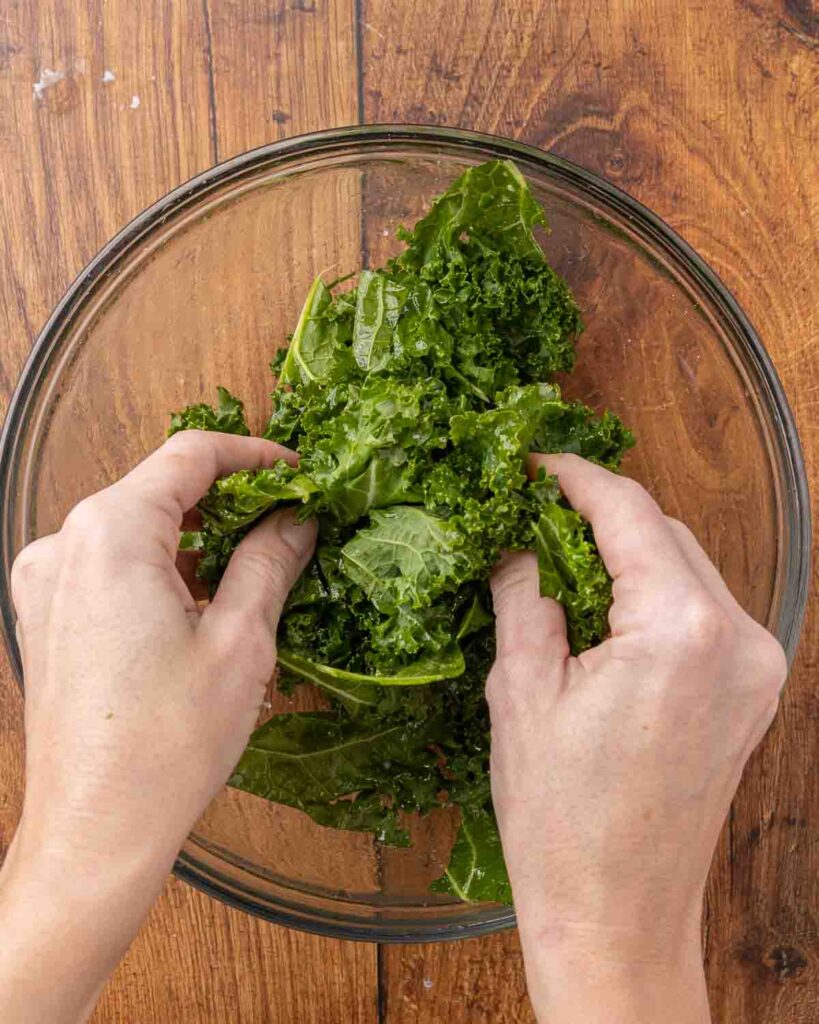 Hands massaging olive oil and spices into fresh kale pieces.