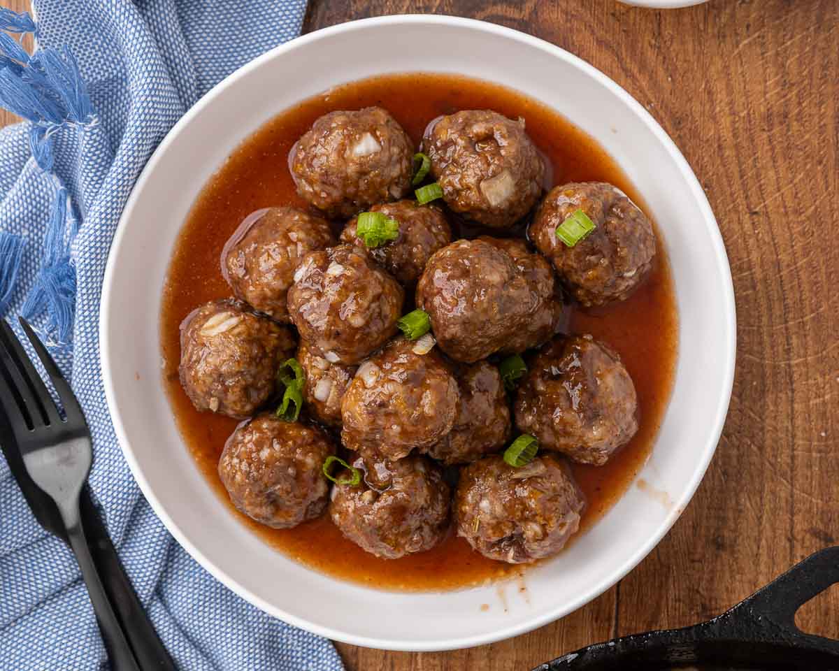 Cocktail meatballs and sauce in a white serving bowl and garnished with scallions.