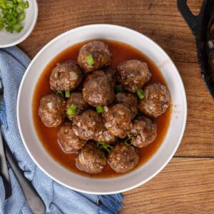 Cocktail meatballs and sauce in a white serving bowl and garnished with scallions.