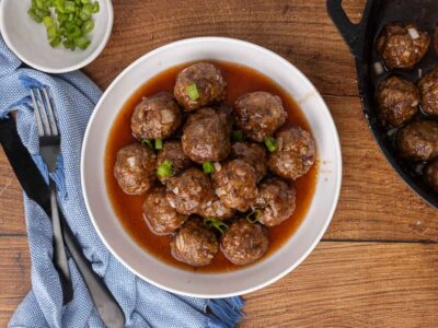 Cocktail meatballs and sauce in a white serving bowl and garnished with scallions.