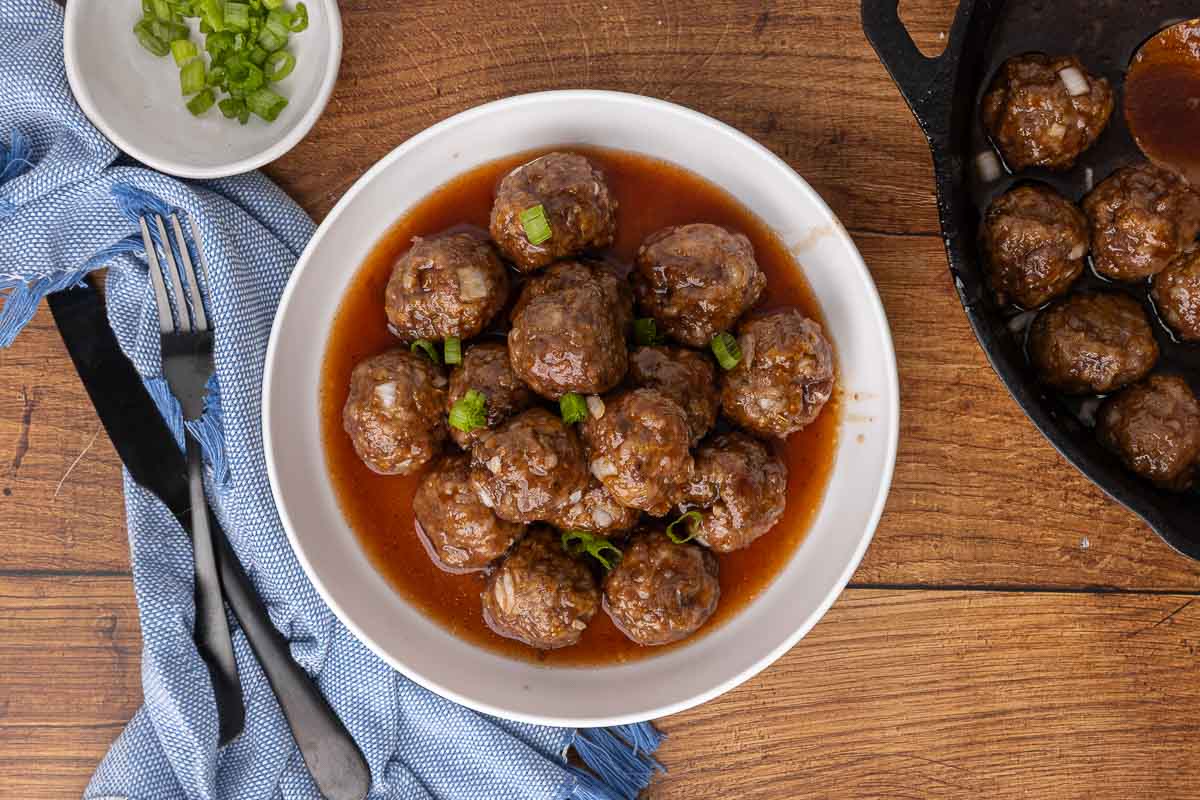 Cocktail meatballs and sauce in a white serving bowl and garnished with scallions.