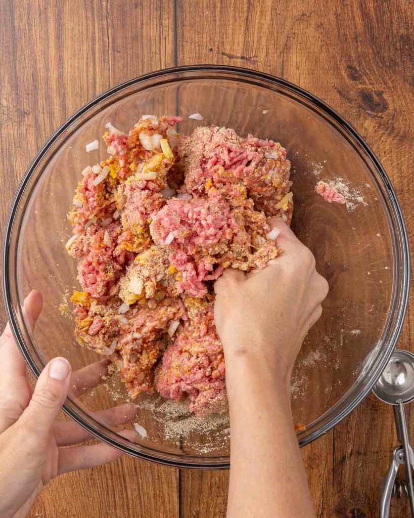 Hands mixing together meatball ingredients in a glass bowl.