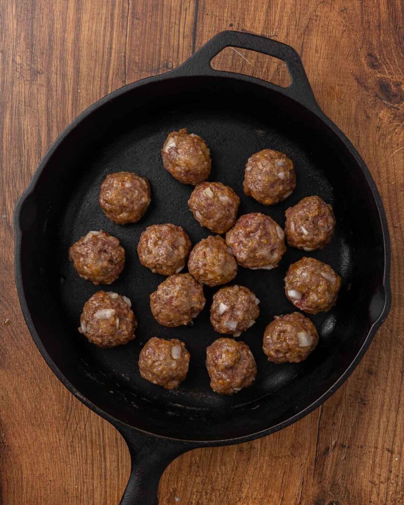 Cocktail meatballs browning in a cast iron skillet.
