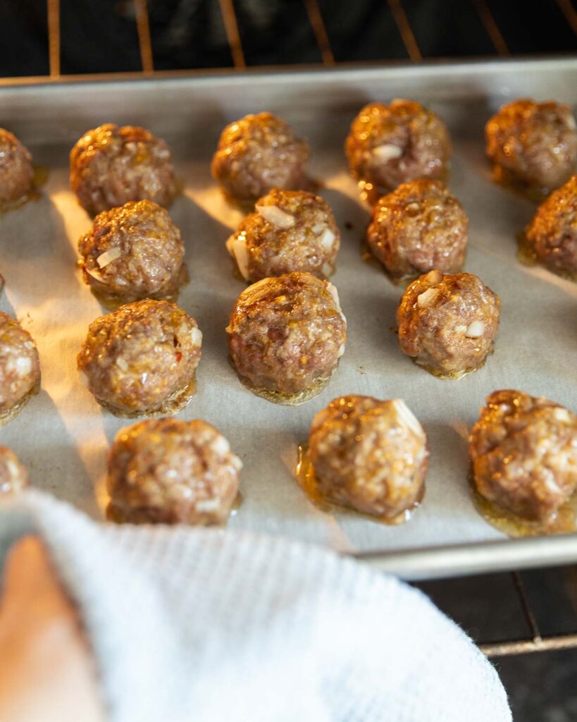 Cocktail meatballs on a baking sheet in the oven.
