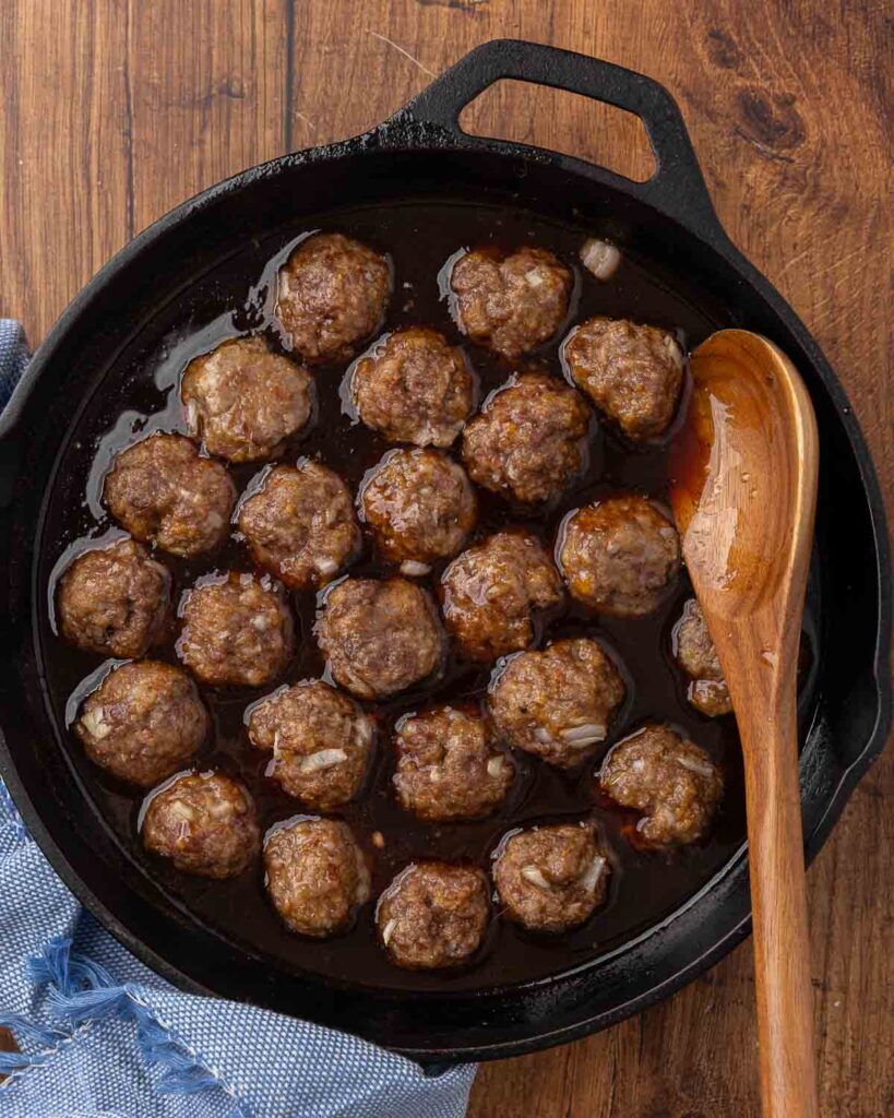 Cocktail meatballs and sauce simmering in a cast iron skillet.