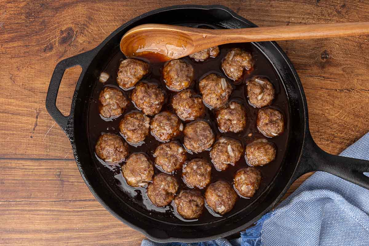 Cocktail meatballs and sauce simmering in a cast iron skillet.