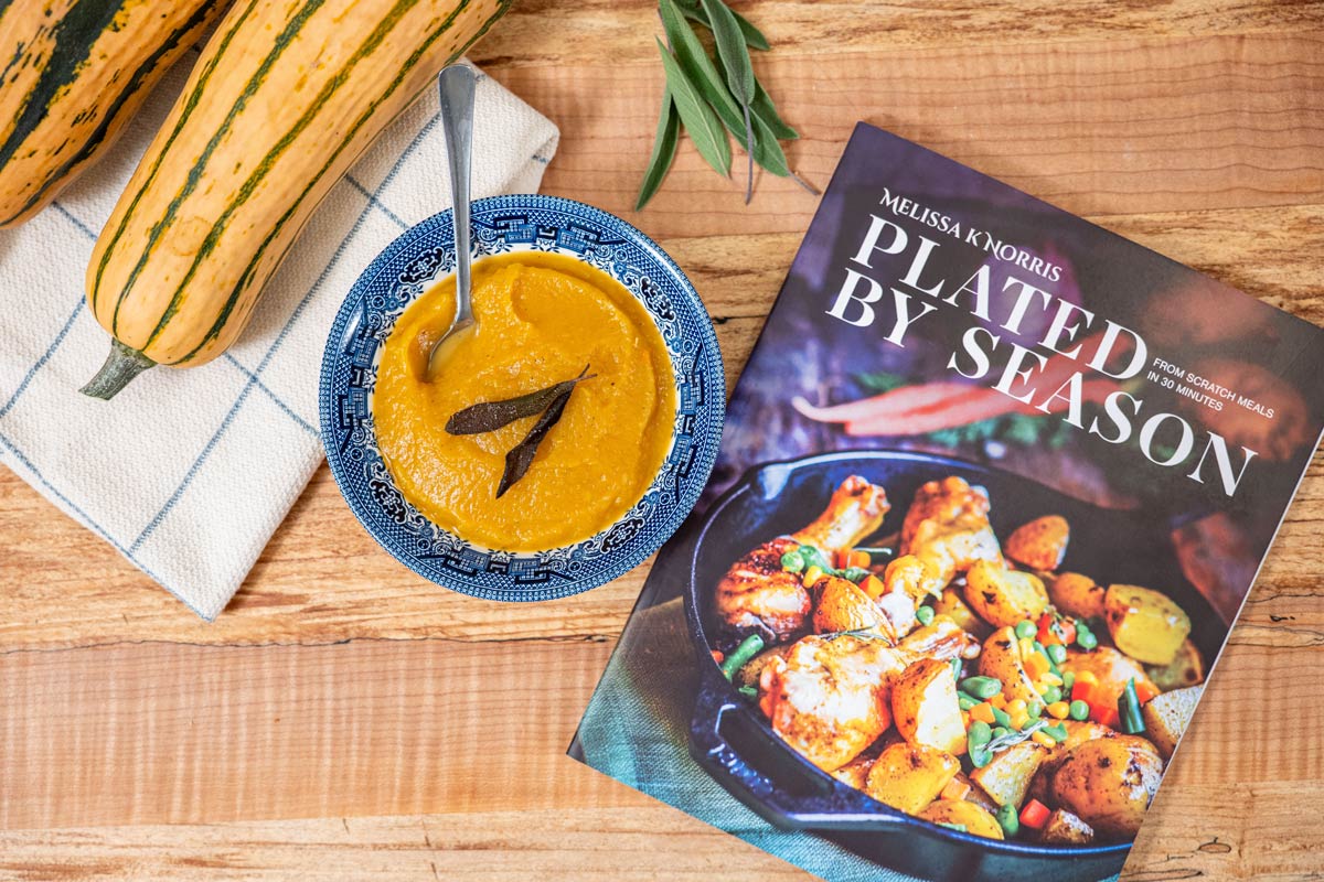 A bowl of Delicata squash soup next to a Plated By Season magazine.